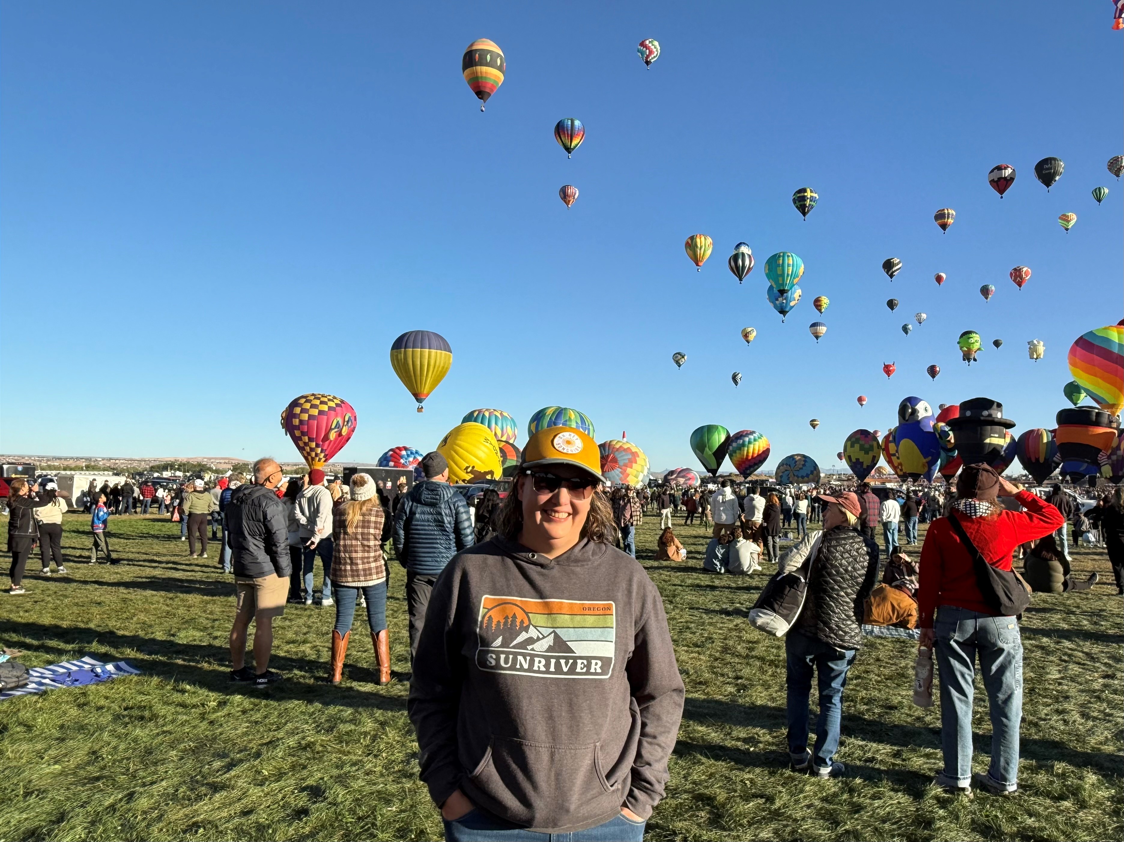 Dr. Elena Griego stands outside, with a group of hot air balloons rising from a field behind her.